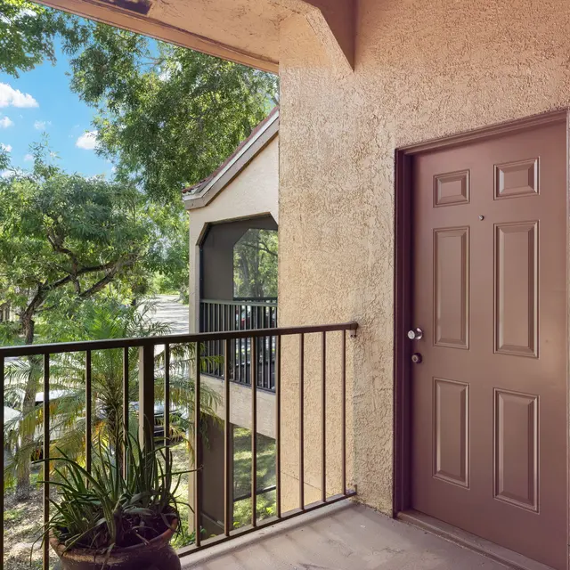 A view from a balcony showing a door with the number 921, surrounded by trees and parked cars below.