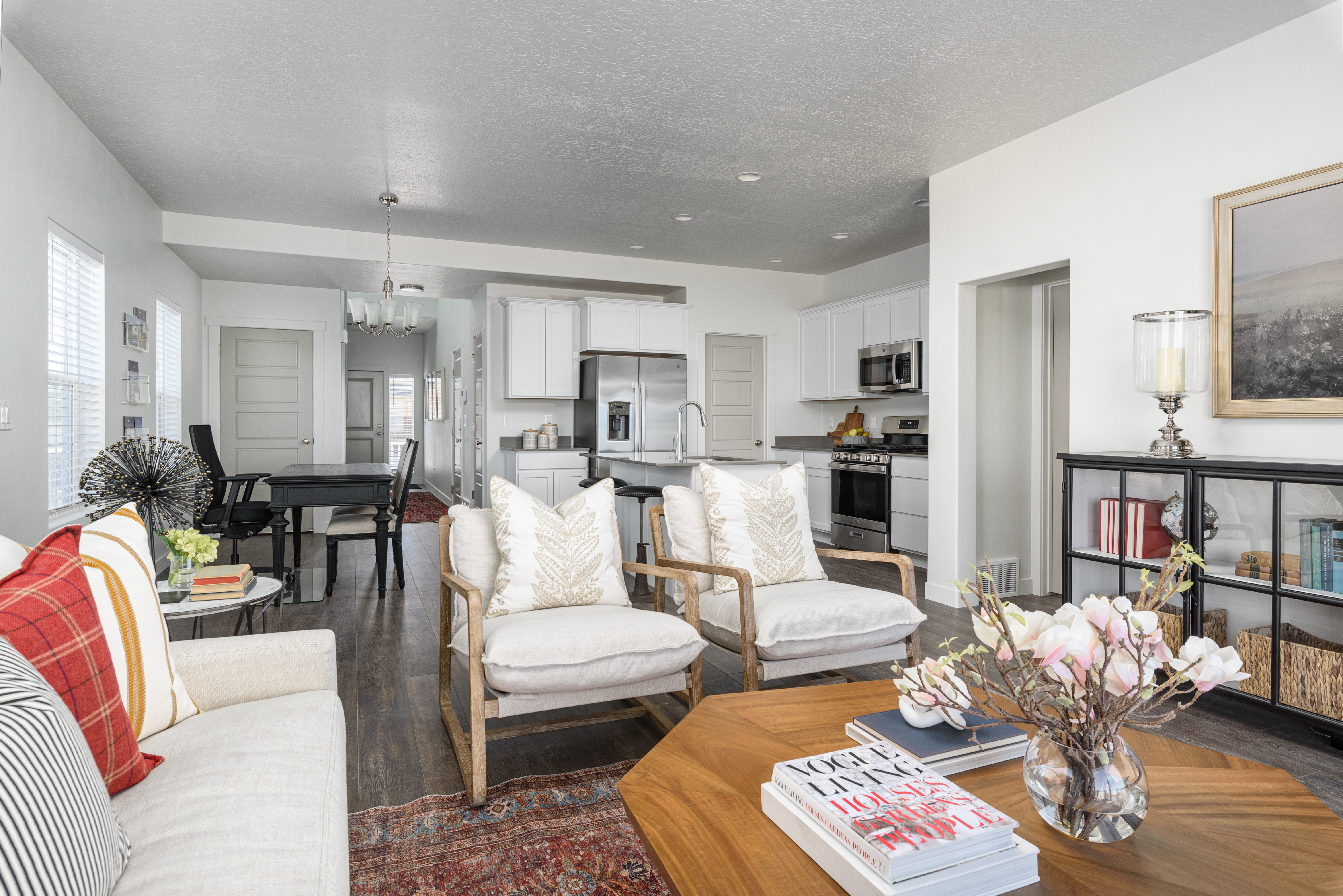 Modern Living Room Interior A modern living room featuring two armchairs and a sofa with decorative pillows, a wooden coffee table, and a vase with flowers. The space includes a dining area in the background, modern kitchen appliances, and light-colored walls.