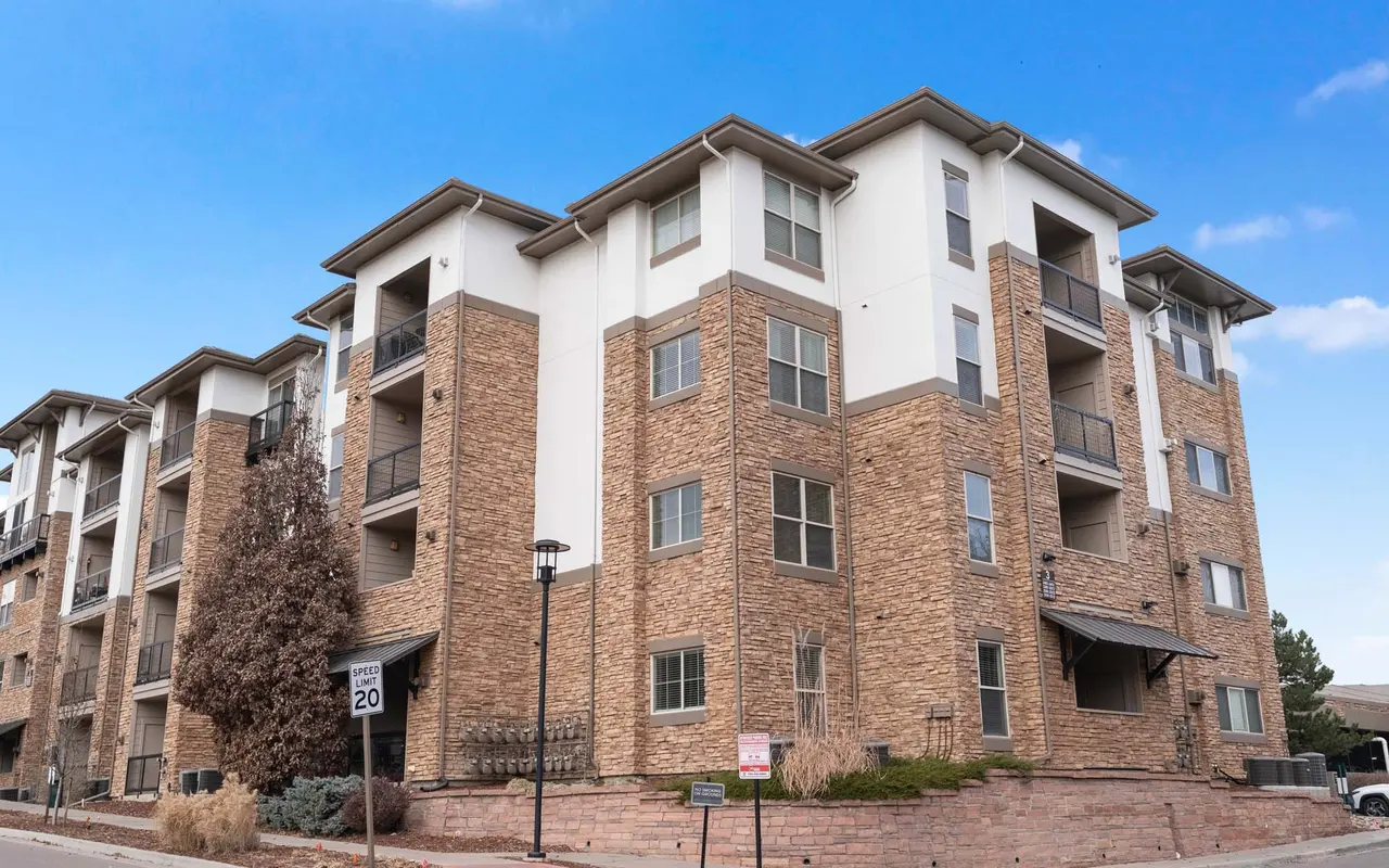 Exterior view of a multi-story apartment building with a stone facade and balconies, against a blue sky.