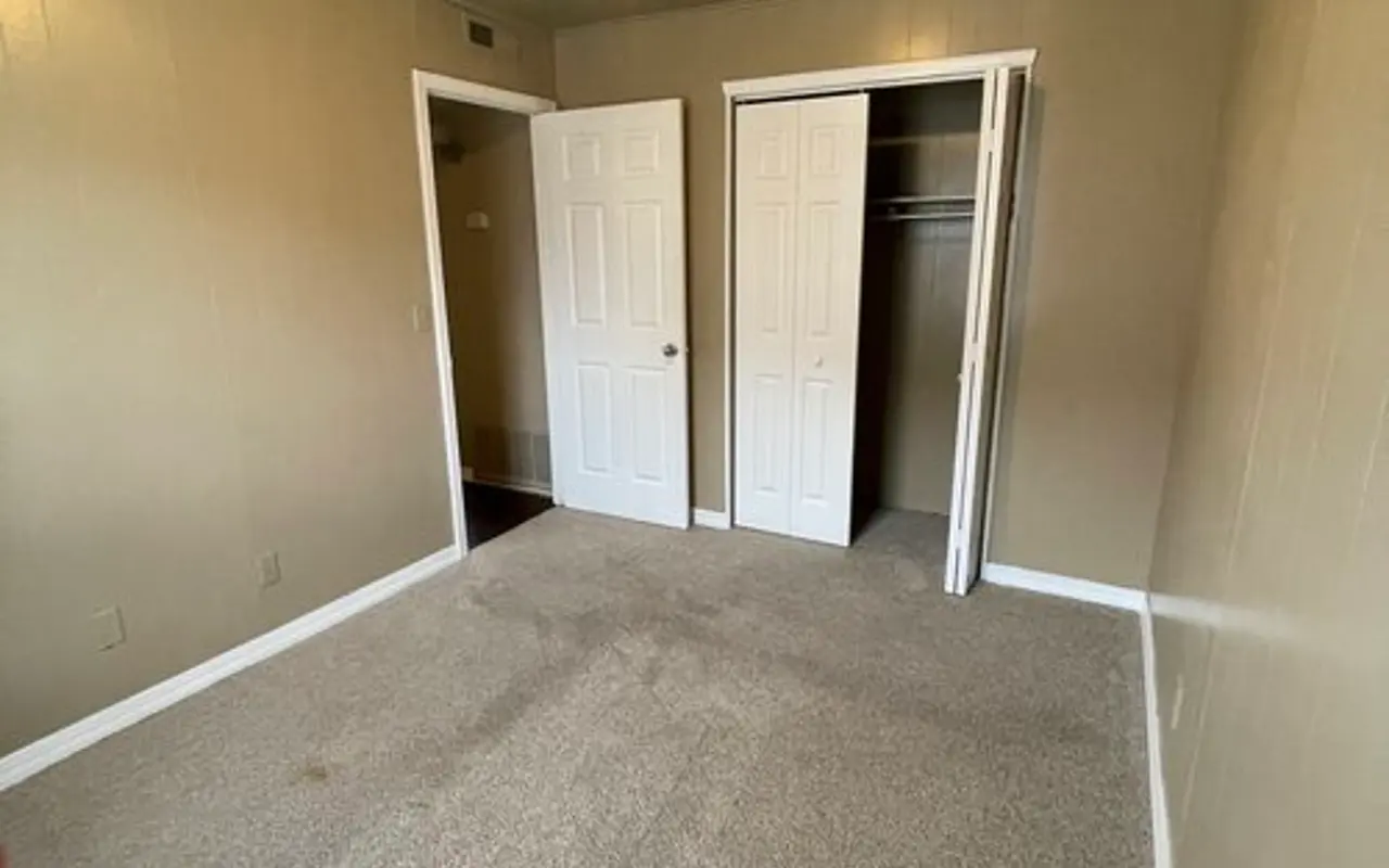Vacant Room Interior A vacant room with beige walls and carpet flooring, featuring two white double doors leading to closets on one side, and a ceiling light fixture.