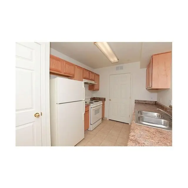 Modern Kitchen Interior A kitchen with light wood cabinets and beige tiled flooring. There is a white refrigerator, stove, and an oven in view, with a sink next to a counter.