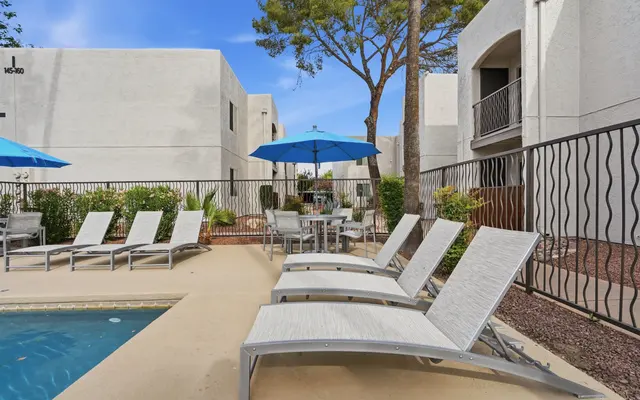 A swimming pool area with lounge chairs and umbrellas surrounded by greenery and apartment buildings in the background.
