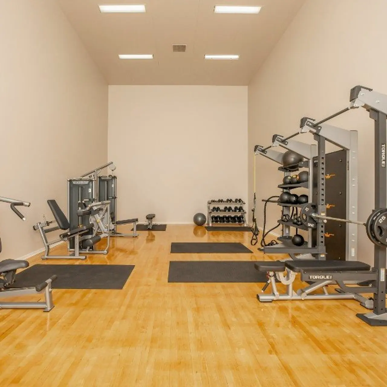 A spacious home gym featuring several workout machines and free weights on a wooden floor.