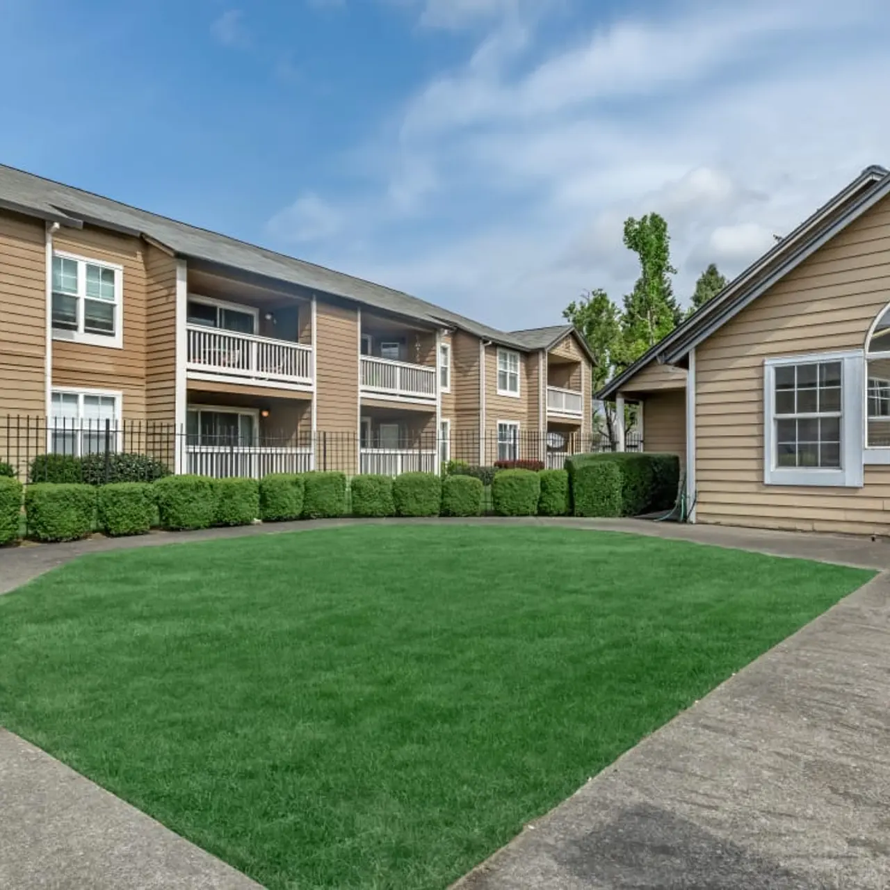 Exterior view of an apartment complex with green lawn, neatly trimmed hedges, and a clubhouse.