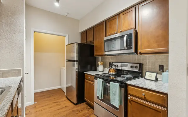 Modern Kitchen Design A modern kitchen with wooden cabinets, stainless steel appliances, and a light granite countertop. A doorway leads to a laundry area.
