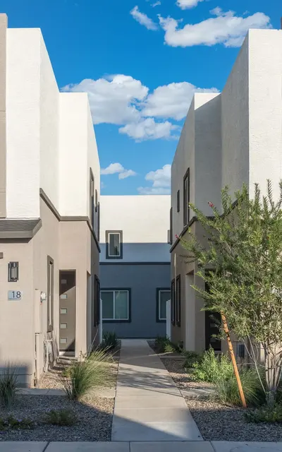 Contemporary Townhouses A row of modern two-story townhouses with gray garage doors and landscaped pathway in between. The sky is blue with fluffy clouds.