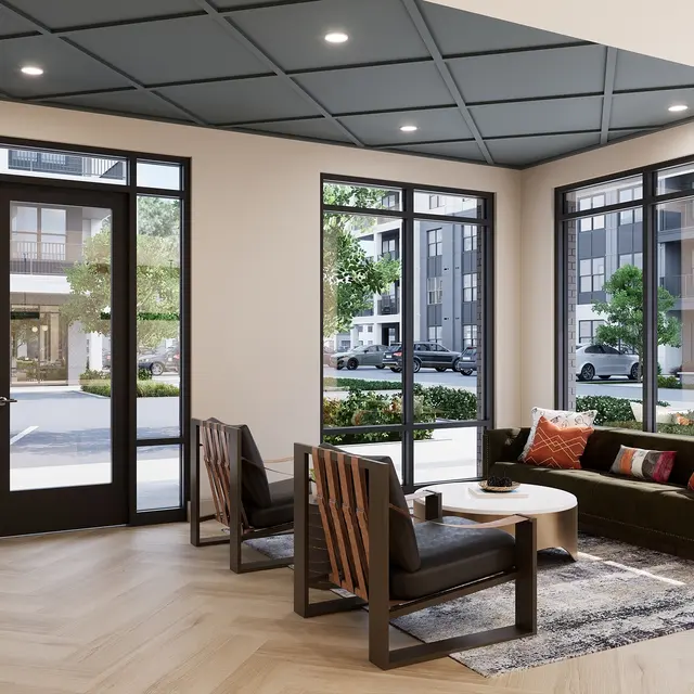 A modern lobby area with large windows and a welcoming atmosphere. It features wooden furniture, a round coffee table, and a cozy seating arrangement.