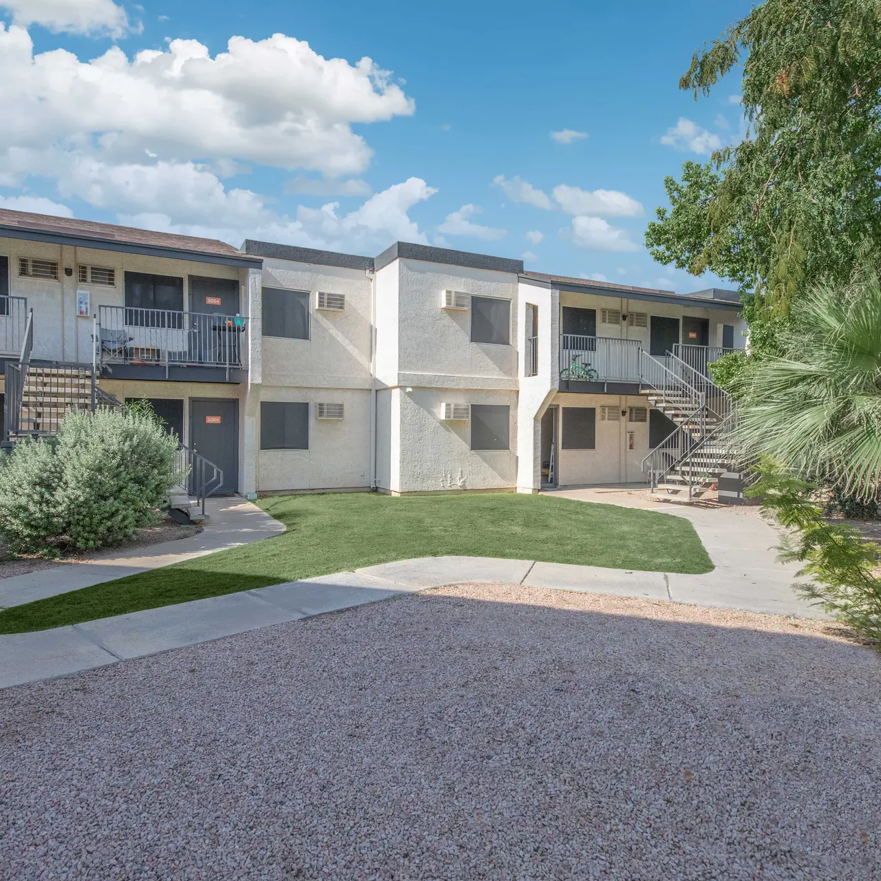 View of an apartment complex with a courtyard, stairs leading to upper levels, and palm trees.