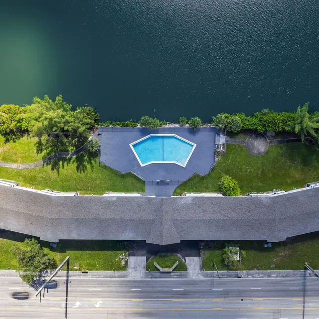 Aerial view of an apartment complex with a pool and surrounding greenery next to a lake.