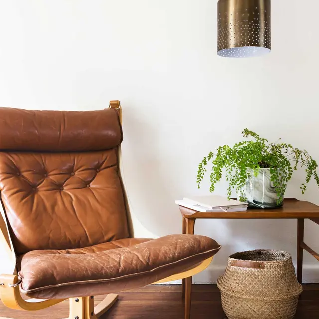 Cozy Living Space with Leather Chair A cozy living space featuring a brown leather lounge chair, a wooden side table with a glass and a potted plant, a woven basket, and a pendant light hanging from the ceiling.