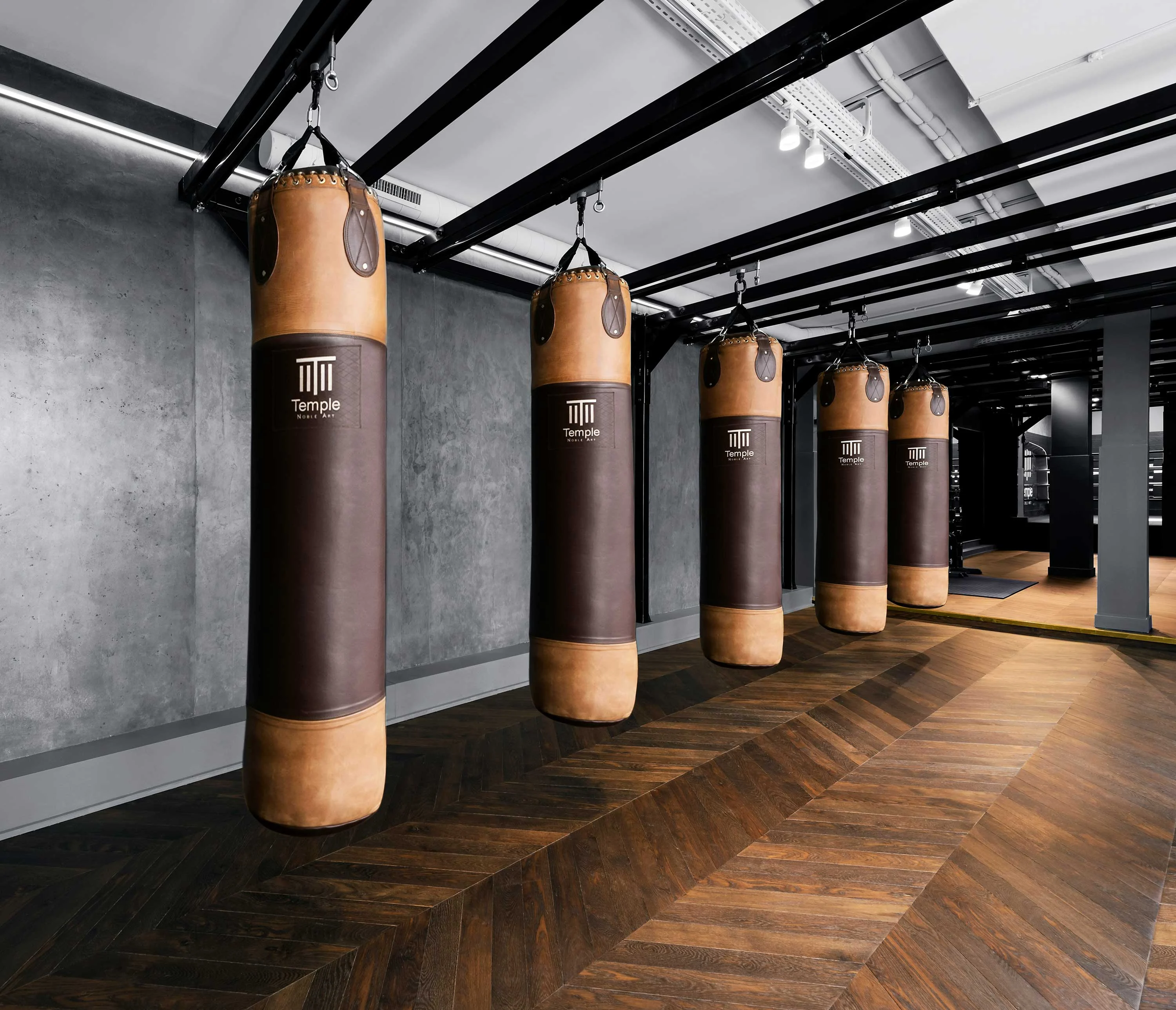 A modern interior of a boxing gym featuring several hanging punching bags against a minimalist backdrop with wooden flooring.