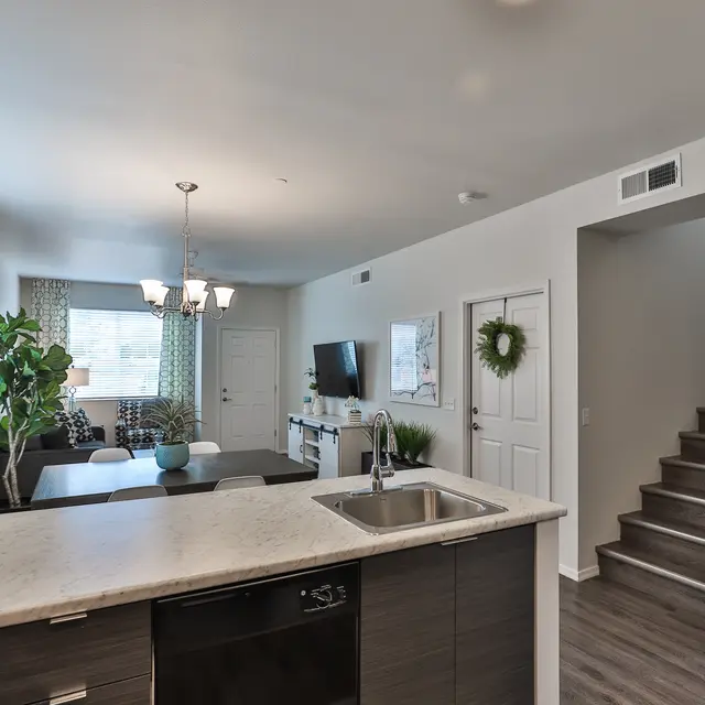 A modern open-plan living room and kitchen area showing a countertop with a sink, a dining table, and a set of stairs leading to another level.