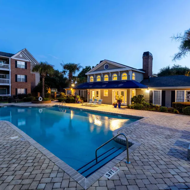 View of an apartment complex with a swimming pool and lounge chairs at dusk.