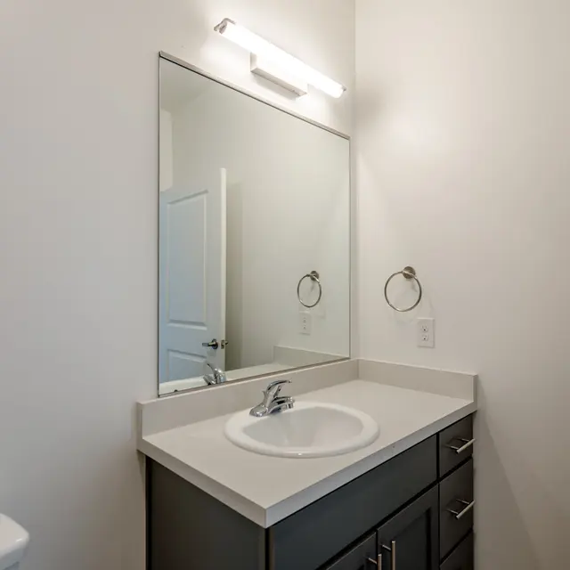 A modern bathroom with a sleek countertop, a round sink, a large mirror, and contemporary fixtures under soft lighting.