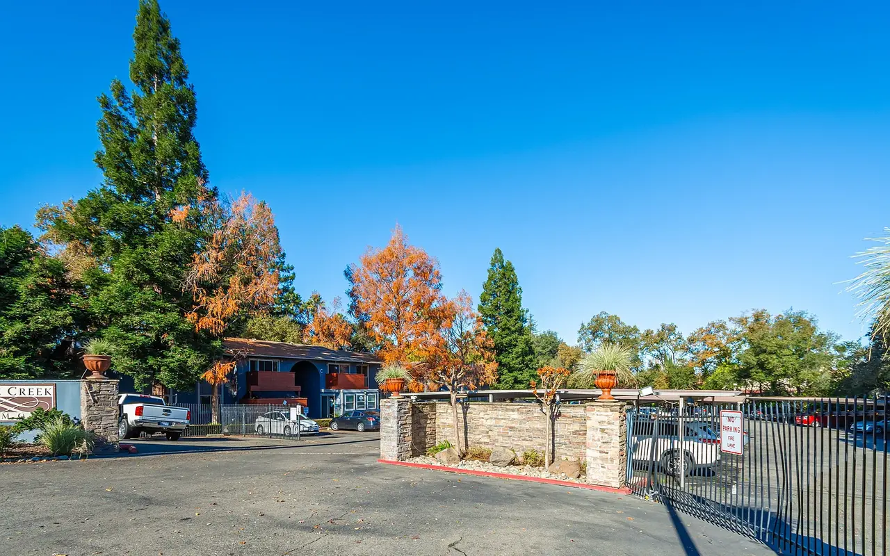 View of the entrance to a property, featuring decorative stone walls and a gated entry, surrounded by trees with vibrant autumn foliage.