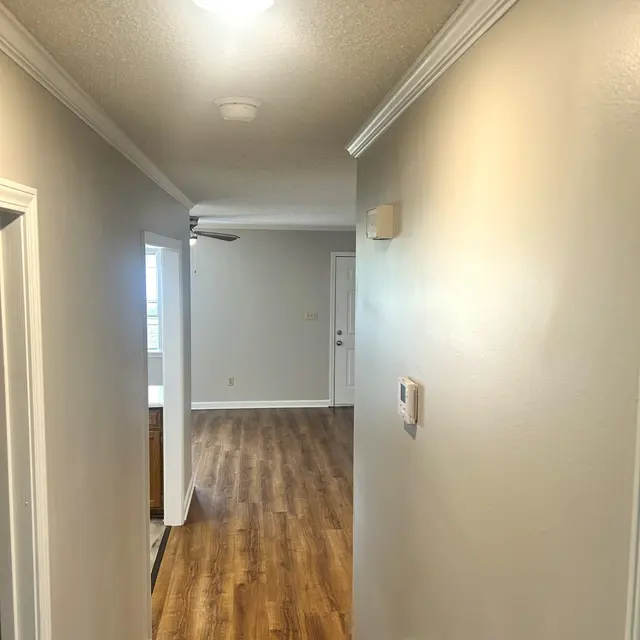 A view down a well-lit hallway with wooden flooring, white walls, and doors on either side.