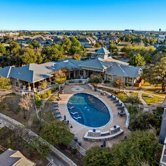 Aerial view of a luxury apartment complex featuring a large pool surrounded by lounge chairs and landscaped gardens.