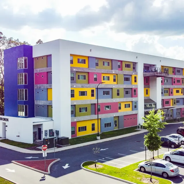 A colorful modern apartment building with a mix of vibrant colors and a landscaped parking area.