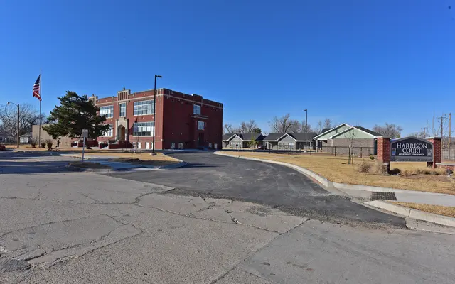 Harrison County Building A view of a brick building with a large parking area and nearby residential houses, under a clear blue sky.