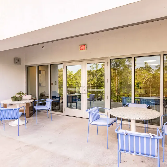 A spacious outdoor seating area with blue chairs and a round table overlooking greenery.