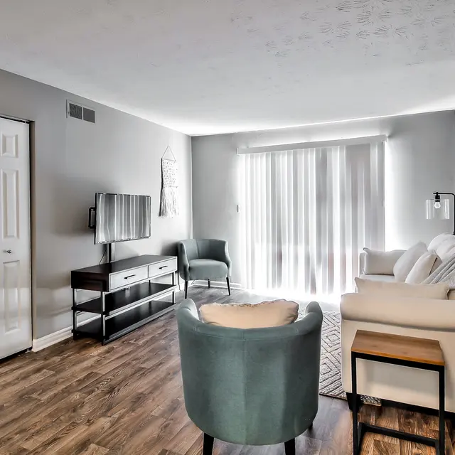 Spacious Modern Living Room A modern living room featuring a light-colored sofa, a teal accent chair, and a TV unit. Large windows let in natural light.