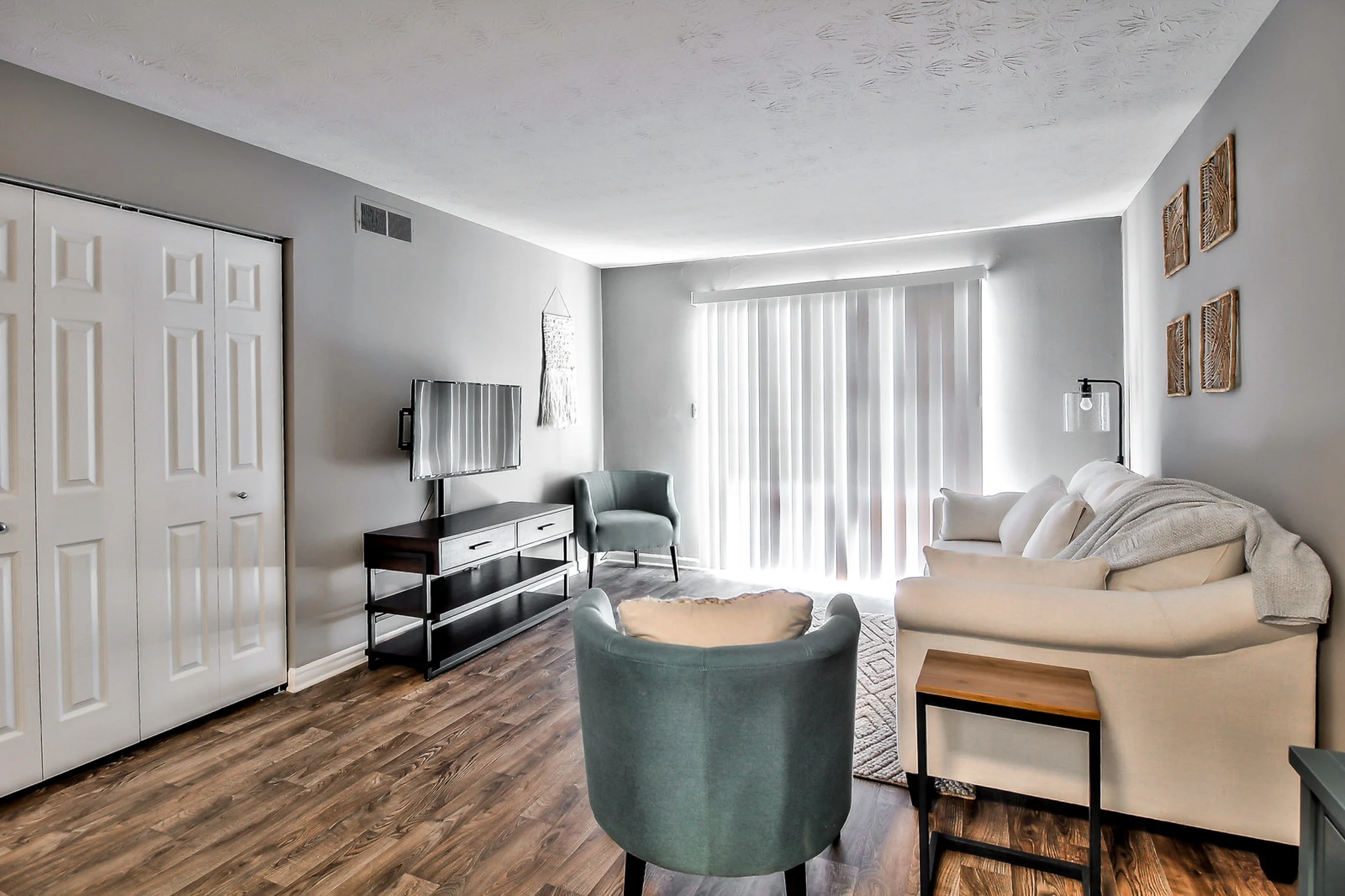 Spacious Modern Living Room A modern living room featuring a light-colored sofa, a teal accent chair, and a TV unit. Large windows let in natural light.