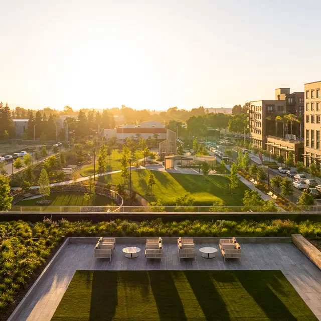 A view of a modern apartment complex with green spaces, walking paths, and a sunset in the background.