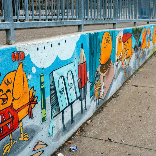 A vibrant mural featuring whimsical cartoon birds and playful objects like a pencil and paintbrush along a sidewalk.