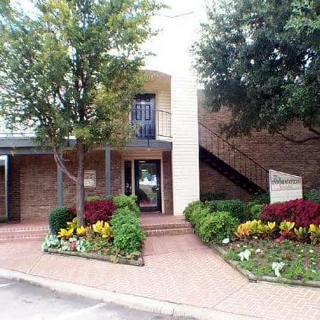 A building entrance with a staircase on the side, surrounded by green shrubs and colorful plants.