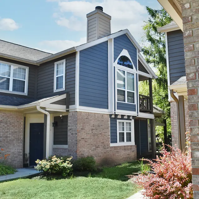 Exterior view of a two-story apartment building with blue siding and a brick base, featuring a chimney and balcony.