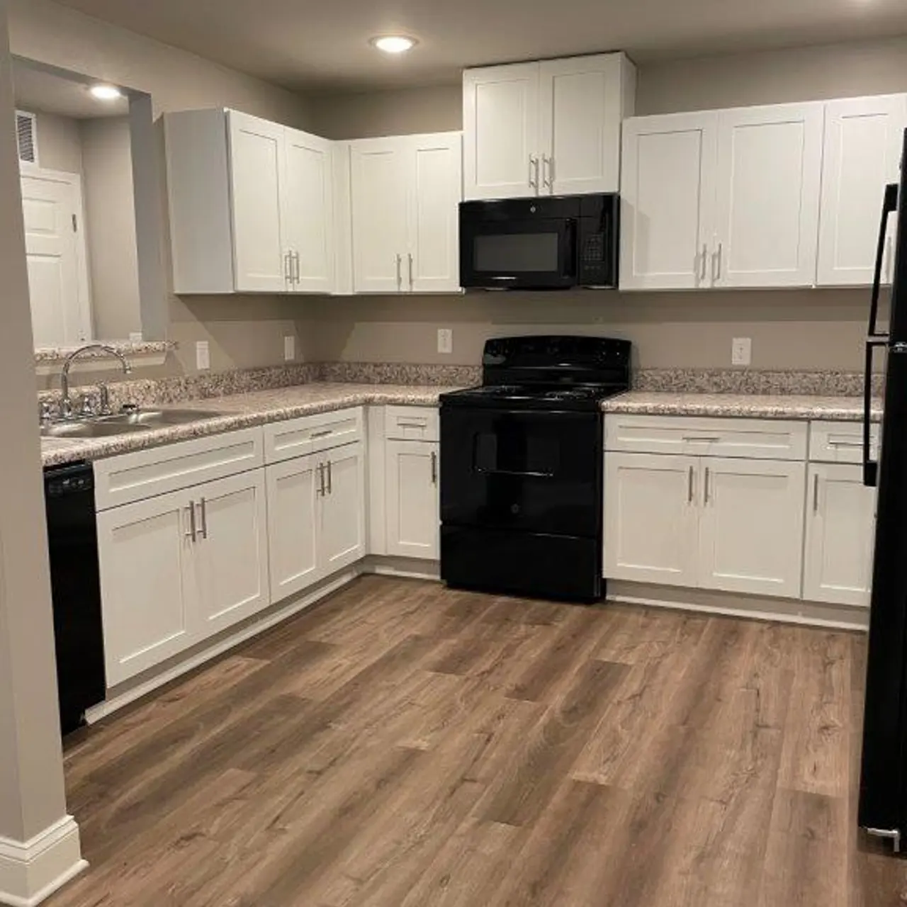A contemporary kitchen featuring white cabinets, a black stove, microwave, and refrigerator, with granite countertops and wooden flooring.