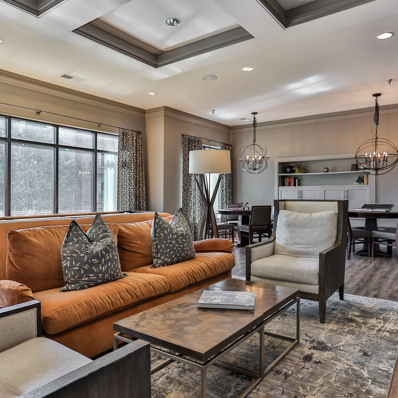 Stylish Modern Living Room A modern living room featuring a brown sofa with patterned cushions, two chairs, a coffee table, and large windows allowing natural light to enter. The decor includes pendant lighting and a dining area in the background.