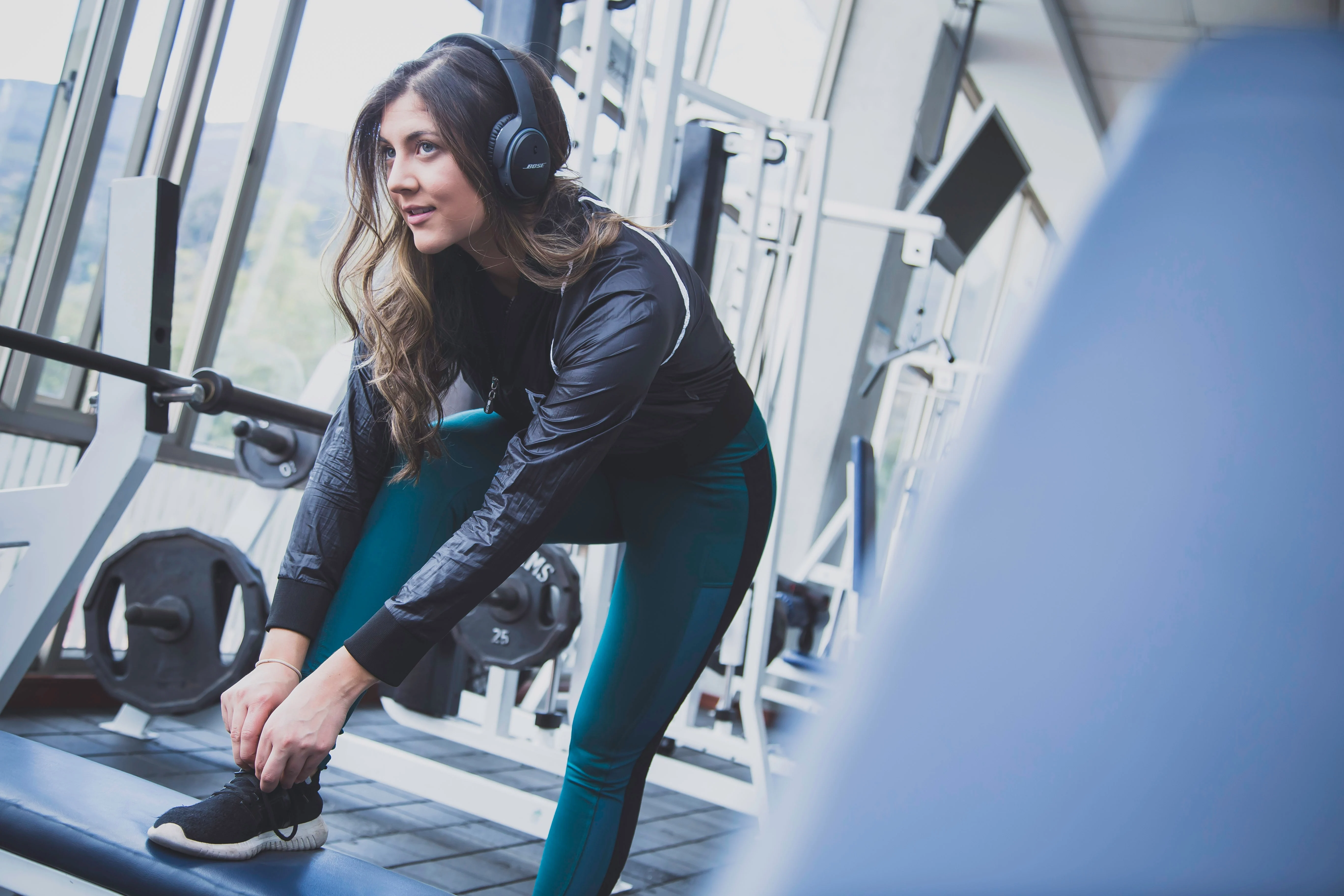 Woman Preparing for Workout in Gym A woman in athletic clothing adjusts her shoelaces while sitting on a bench in a gym environment with exercise equipment in the background.