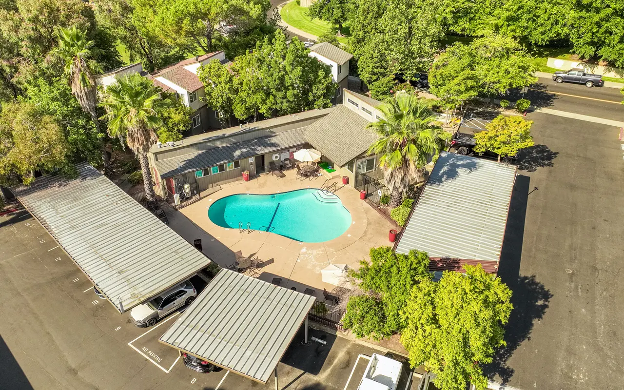 Aerial view of a residential area featuring a swimming pool surrounded by greenery and parking spaces.