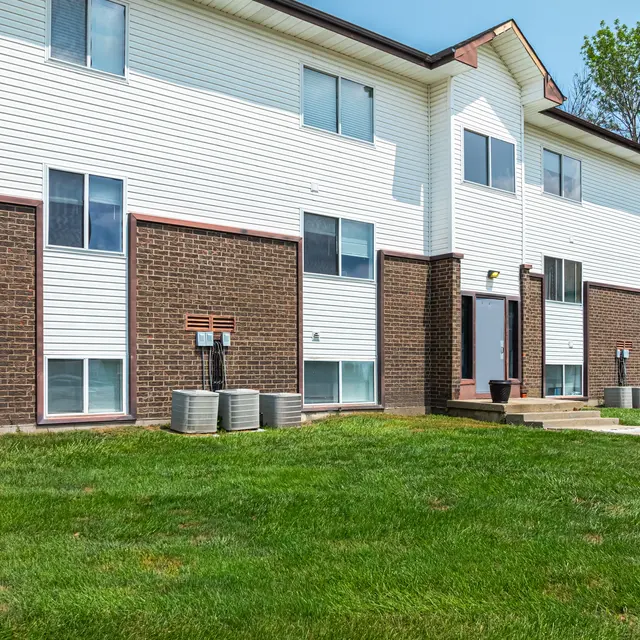 Apartment Building Exterior A view of a two-story apartment building facade with brick and white siding, featuring a green lawn in front.