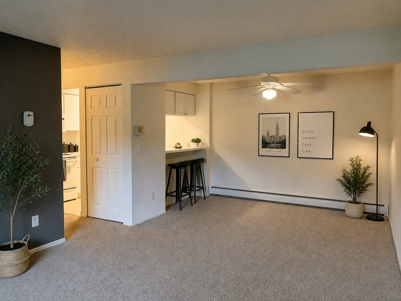 A spacious living area in a modern apartment with a carpeted floor, bar seating, and framed wall art.