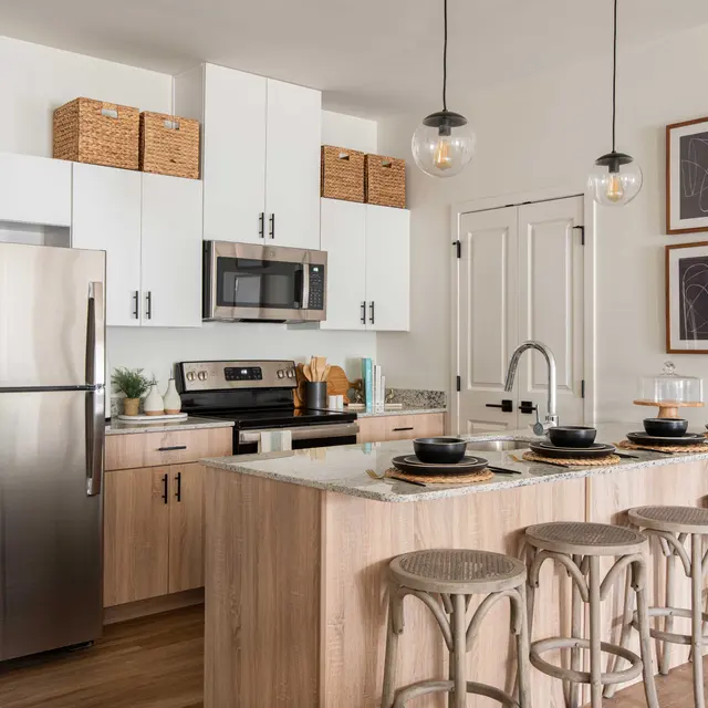 A modern kitchen featuring light-colored cabinetry, stainless steel appliances, an island with seating, and decorative wall art.
