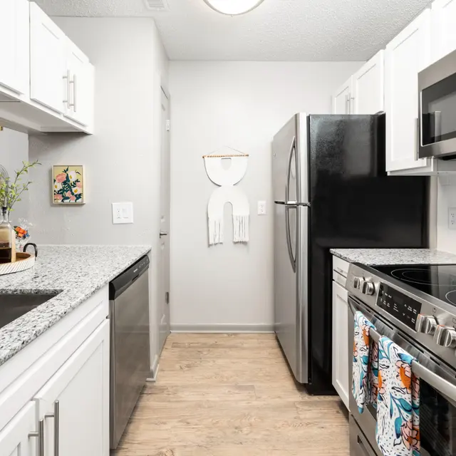 Modern kitchen with white cabinets, granite countertops, stainless steel appliances, and a wooden floor. Bright and minimalist design.