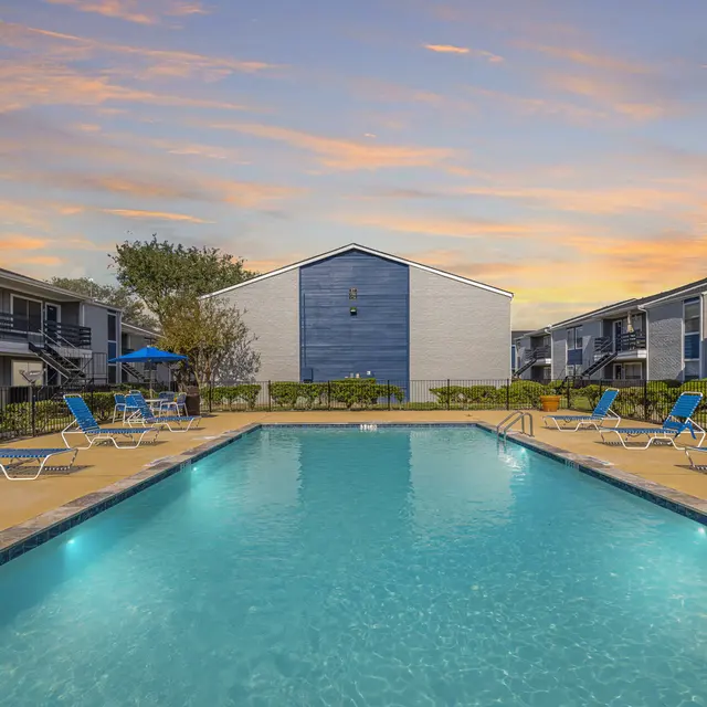 Evening Poolside at Apartment Complex A swimming pool surrounded by lounge chairs in an apartment complex setting during sunset.