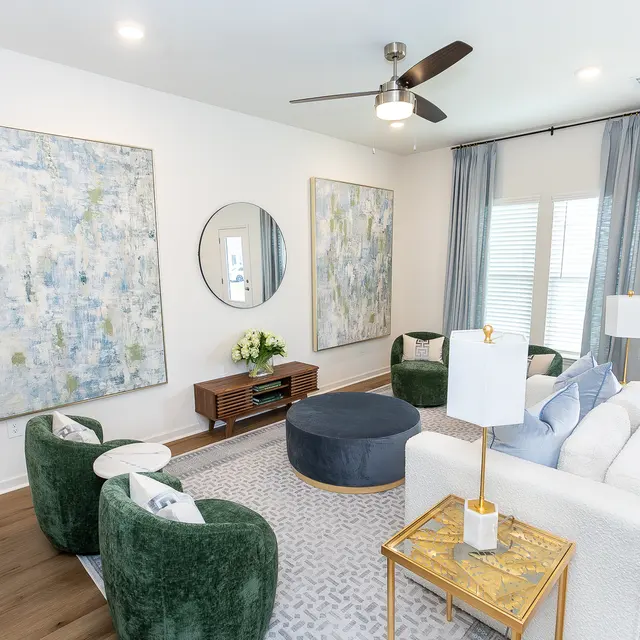 Modern living room featuring green chairs, a white couch, a round coffee table, and two large abstract paintings on the wall.
