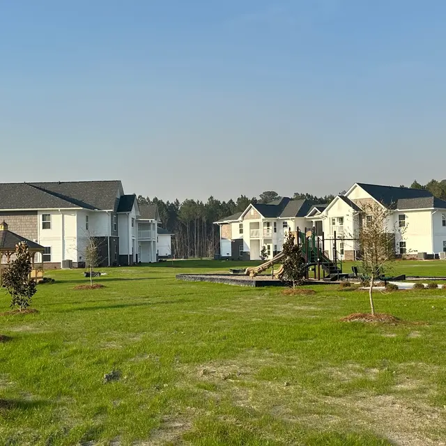 A view of a suburban area with multiple white homes, a playground, and grassy lawns under a clear blue sky.
