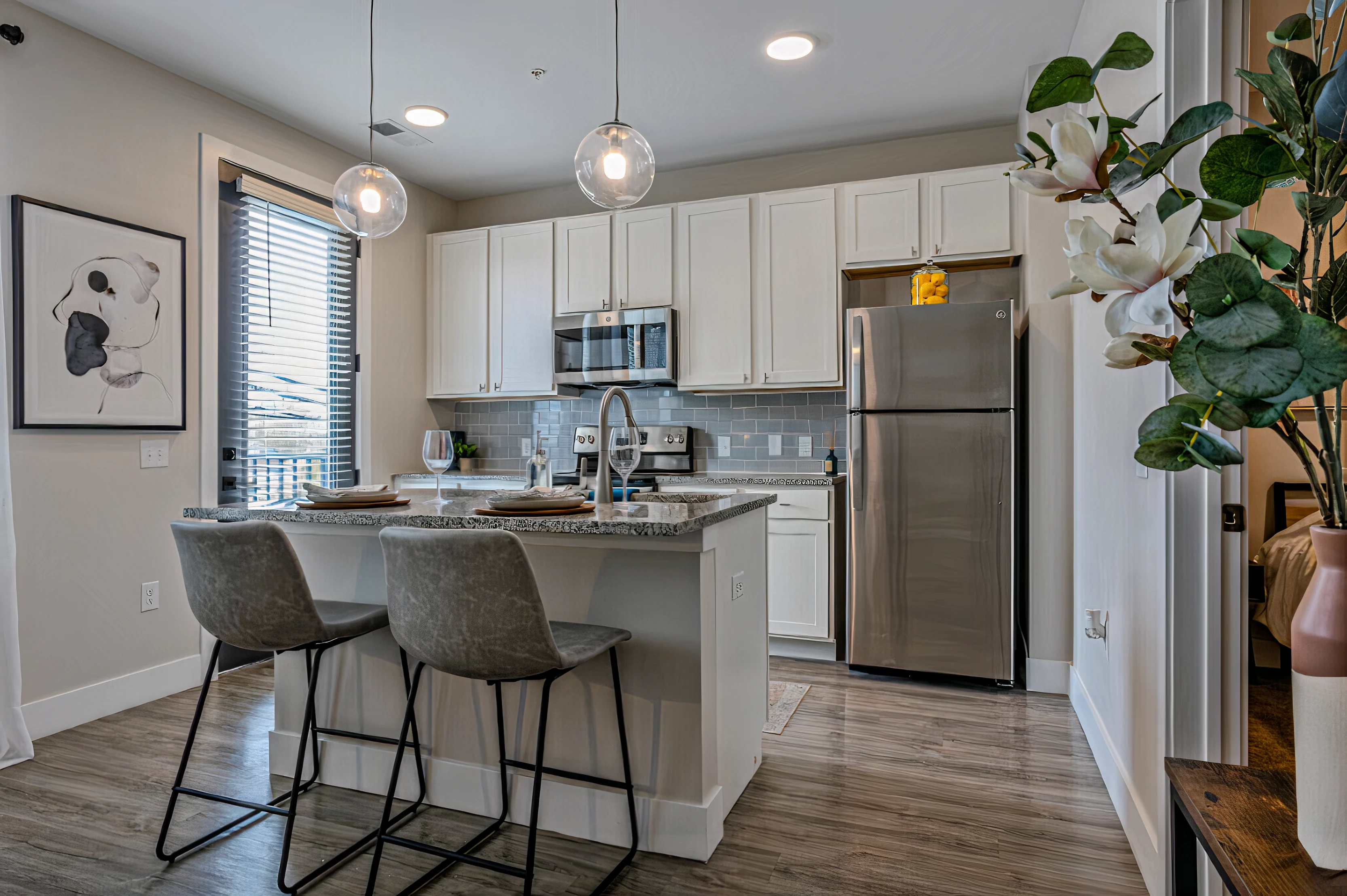 A modern kitchen featuring a minimalist design with light cabinets, stainless steel appliances, an island with seating, and decorative plants.
