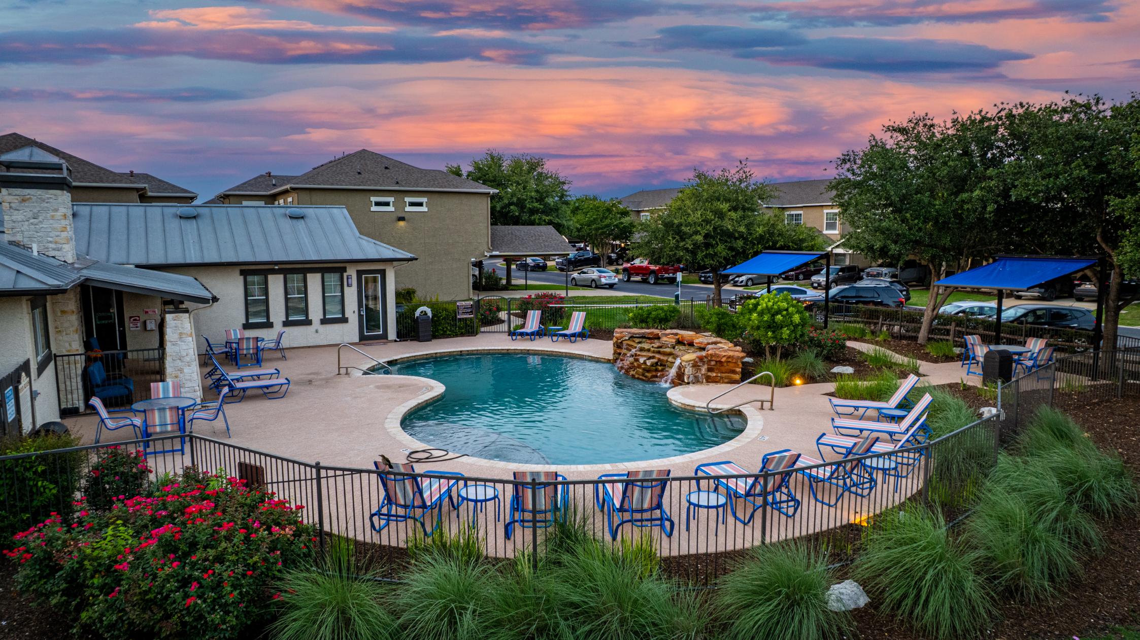 Scenic Pool Area at Sunset A picturesque pool area surrounded by lounge chairs, gardens, and trees, with a colorful sunset in the background.