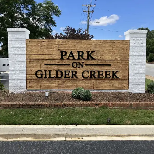 Sign for Park on Gilder Creek, featuring wooden panel and greenery in front.