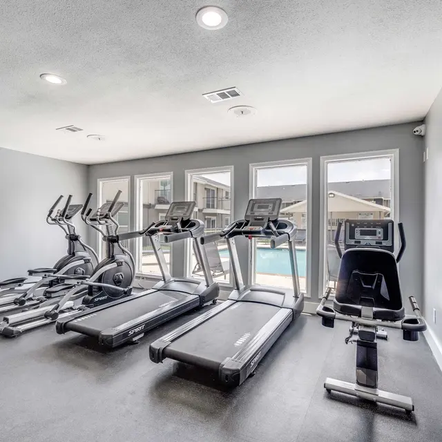 Fitness center with recessed overhead lighting, workout equipment such as stationary bike, treadmills, and ellipticals looking out at resident pool at North Star Apartments