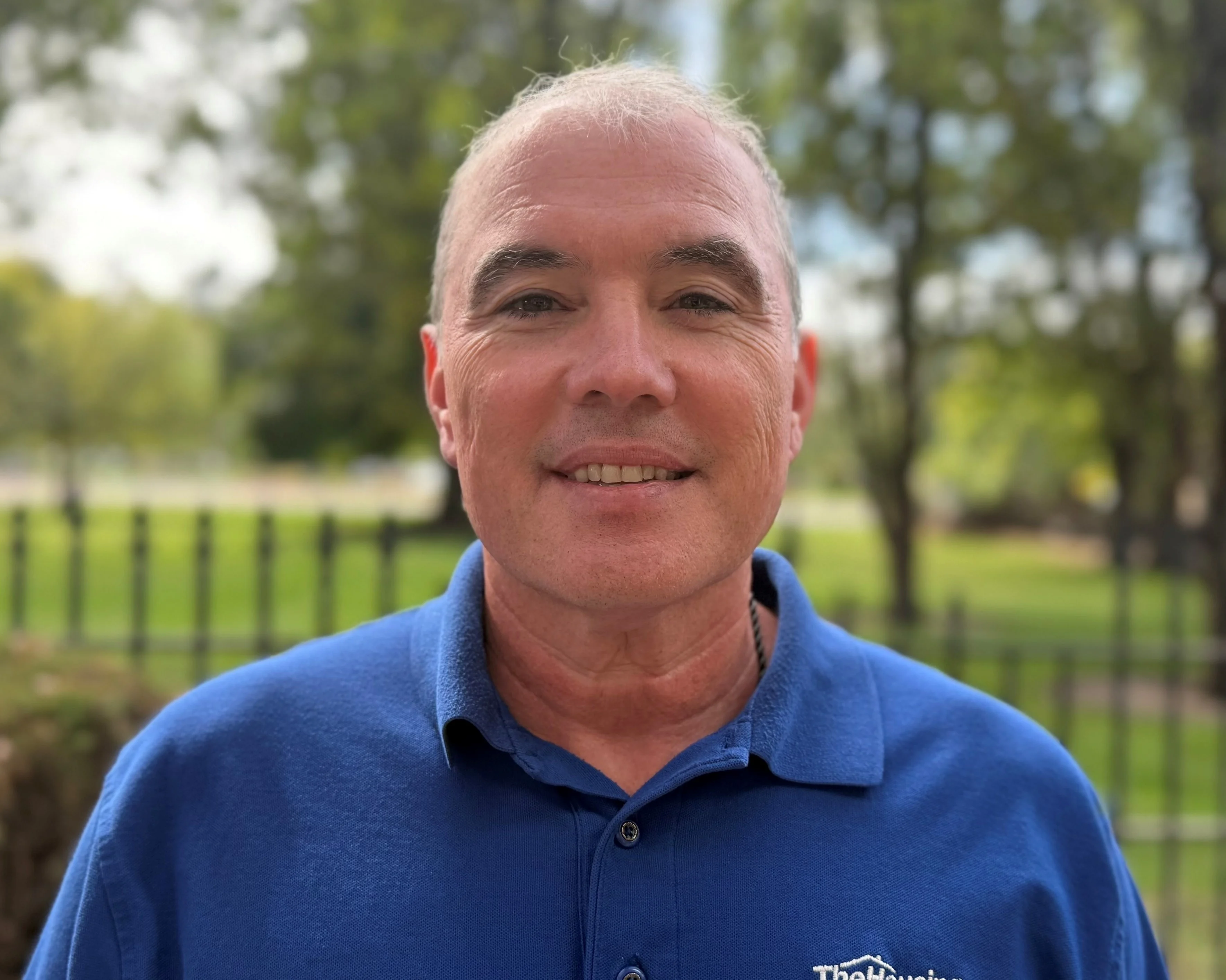 Outdoor Portrait of a Man A man smiling outdoors in a blue shirt, with green trees in the background.