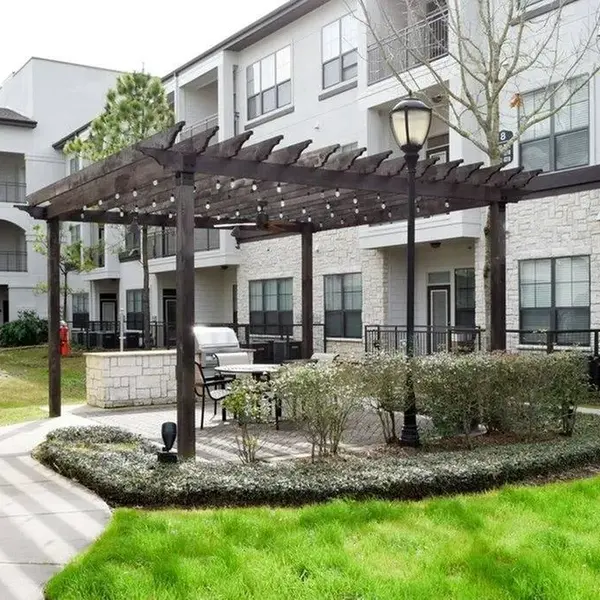 Exterior of Palazzo at Cypresswood Apartments with wooden pergola, seating beneath, and grassy area all around it