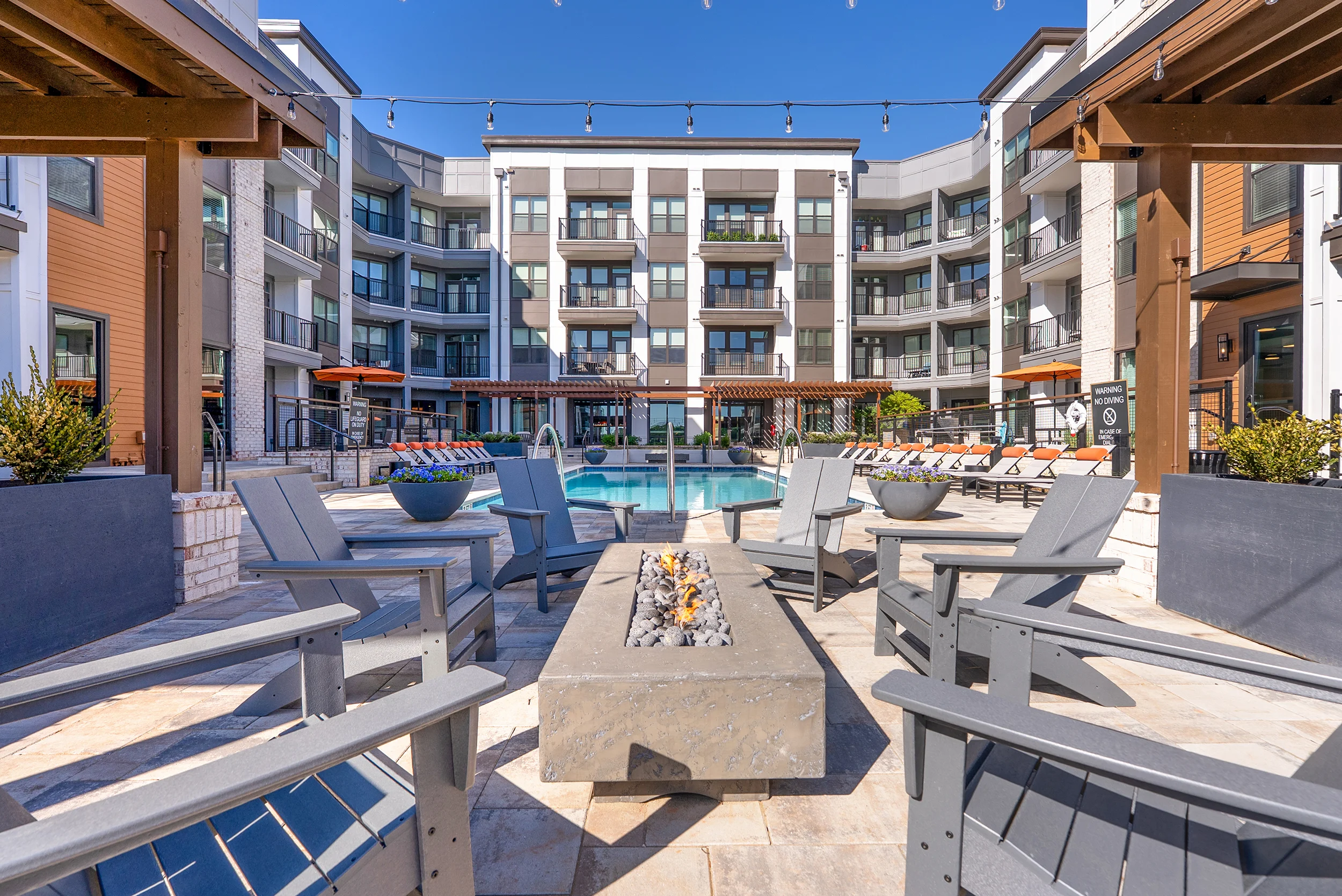 A modern apartment complex courtyard featuring a pool, outdoor seating with fire pits, and landscaped areas.