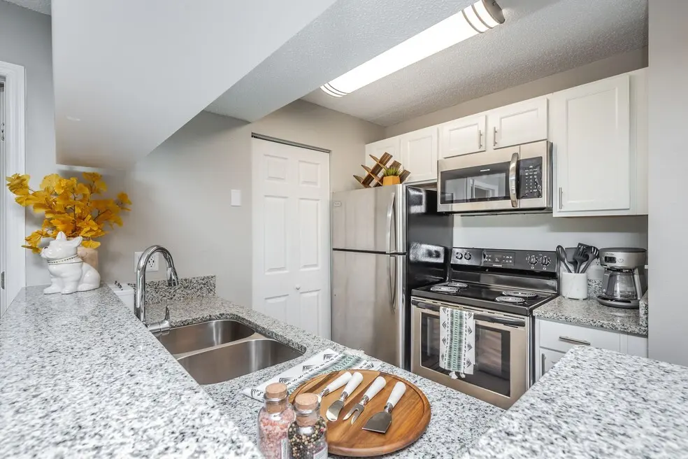 Atwater at Westchase Modern kitchen featuring stainless steel appliances, granite countertops, and decorative elements like a flower arrangement and utensils.