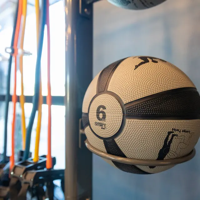 A close-up of a black and white exercise ball on a storage rack, with colorful resistance bands hanging in the background.